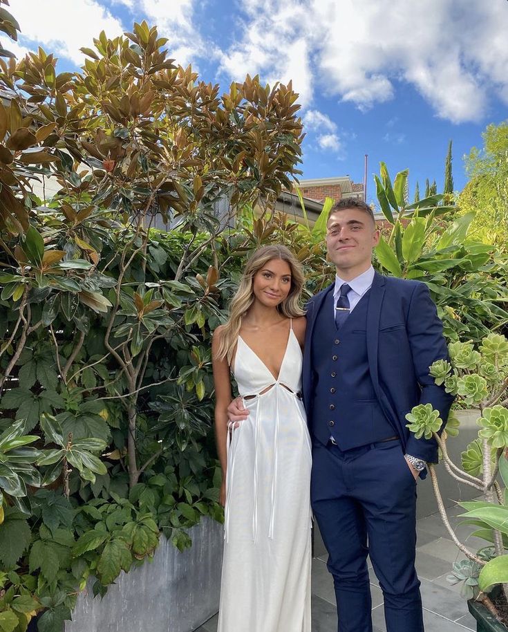 a man and woman standing next to each other in front of some bushes with trees