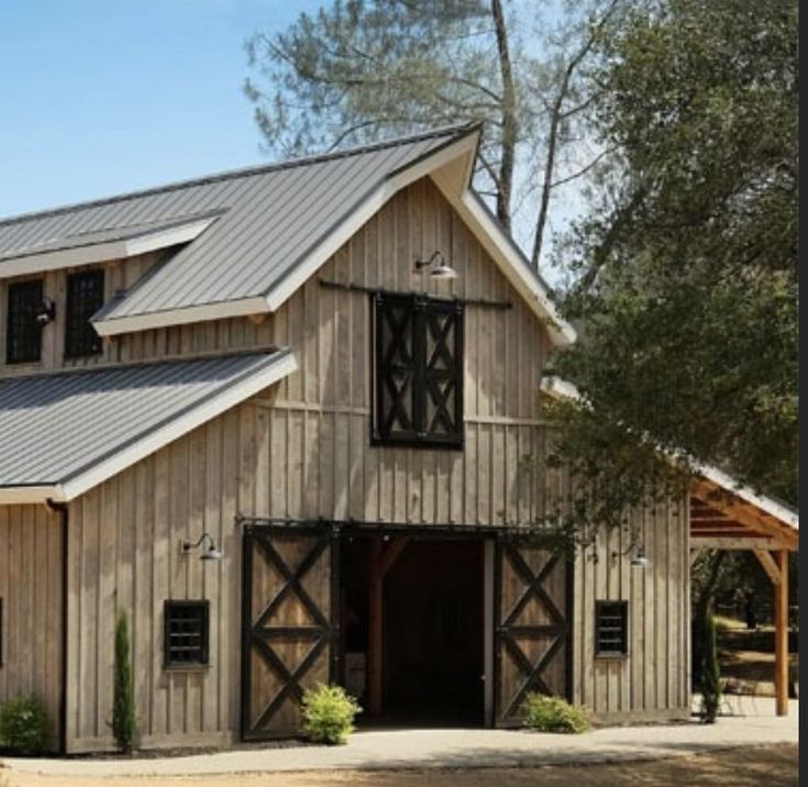 an old barn with a metal roof and two doors on the front, surrounded by trees