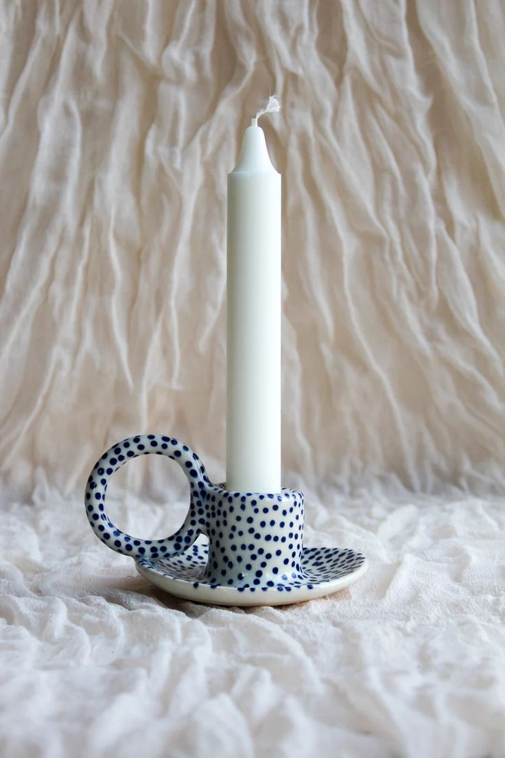 a white candle sitting on top of a saucer next to a black and white polka dot ribbon