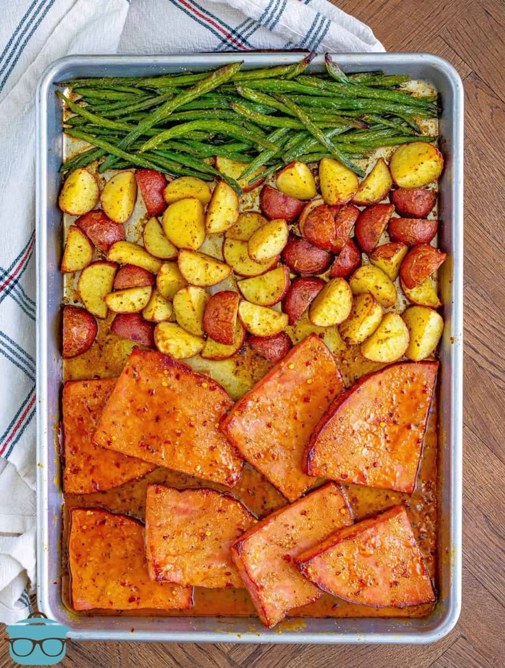 a pan filled with potatoes, green beans and other food on top of a wooden table