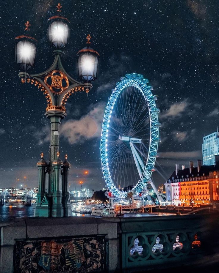 a large ferris wheel sitting next to a street light on top of a bridge under a night sky filled with stars