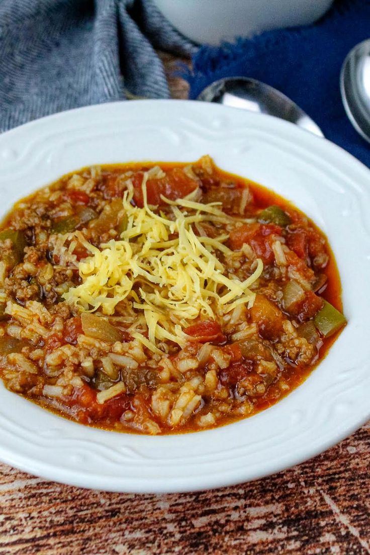 a white bowl filled with chili and rice on top of a wooden table next to silverware