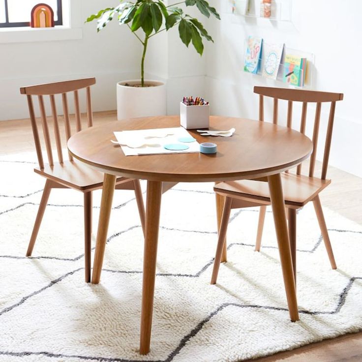 three wooden chairs around a round table in a room with white carpet and potted plant