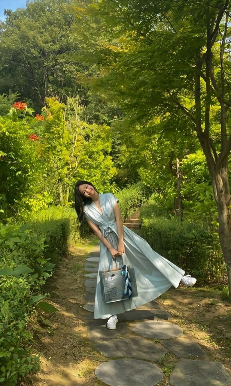 a woman in a blue dress walking down a path with a handbag on her shoulder