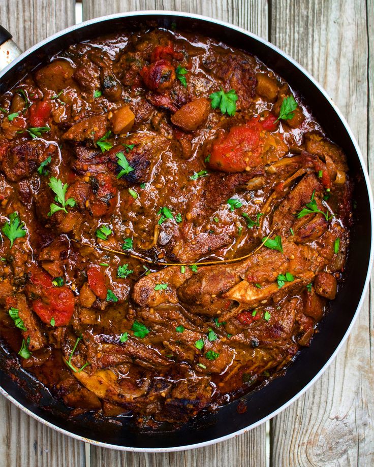 a skillet filled with meat and vegetables on top of a wooden table next to a spoon