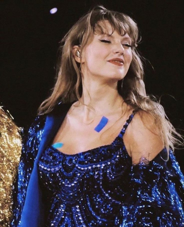 a woman wearing a blue and gold dress with her eyes closed while standing in front of a microphone