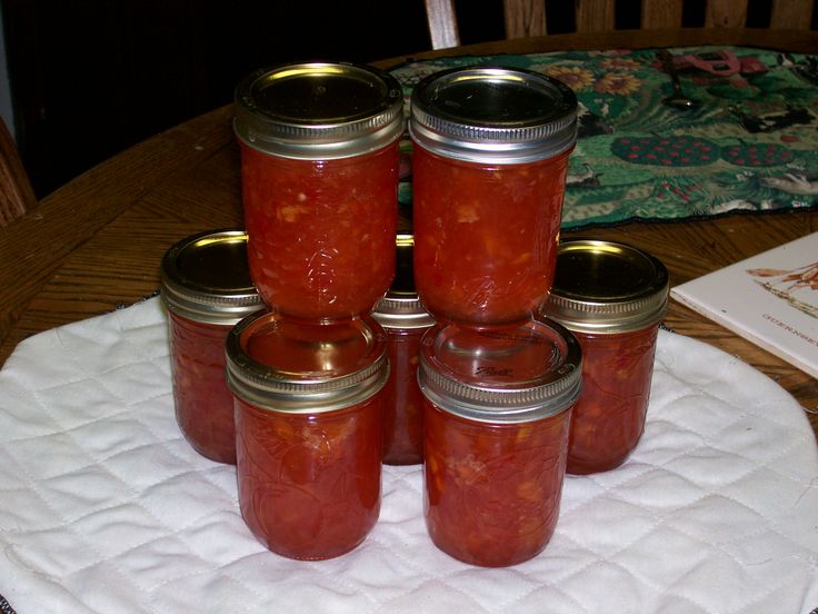 four jars filled with red liquid sitting on top of a white cloth covered placemat