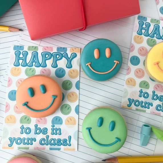 decorated cookies with happy faces on them next to notebooks and pencils for teachers