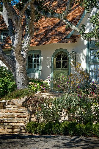 a white house with green shutters next to a tree