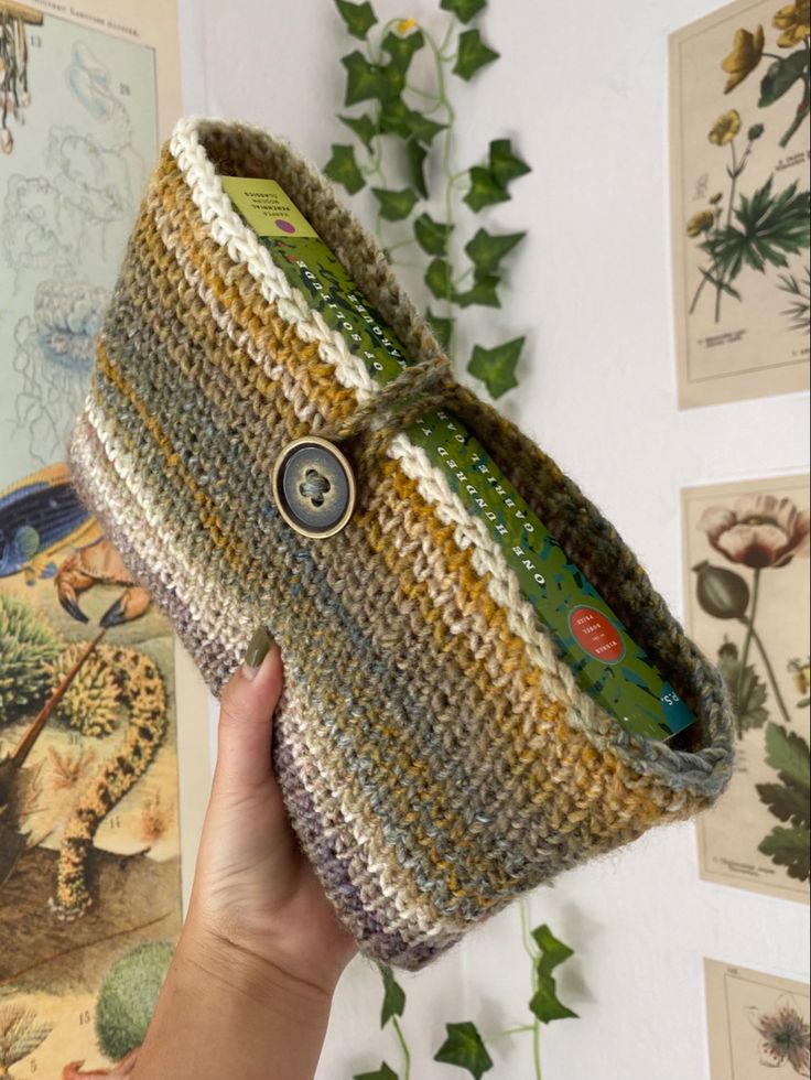 a hand holding up a knitted purse in front of wall with pictures on it