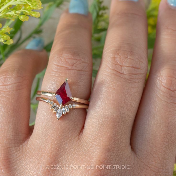 a woman's hand wearing a gold ring with a red and white stone on it