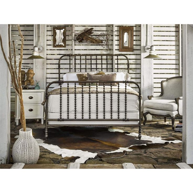 a bedroom with white walls and an antique iron bed frame in the middle, surrounded by cow hide rugs