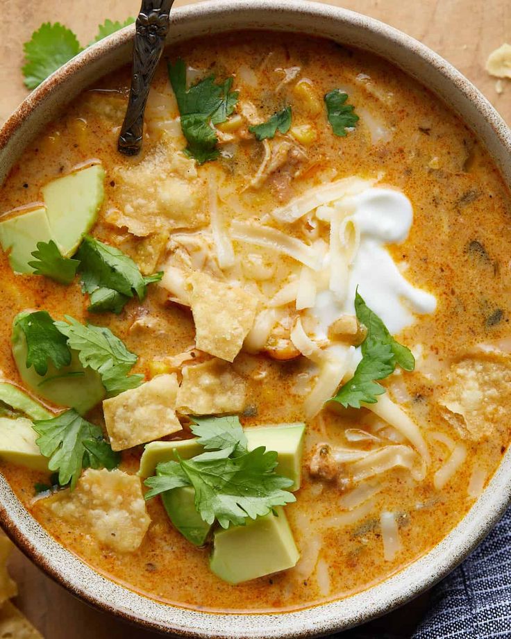 a bowl of soup with tortilla chips and avocado garnish