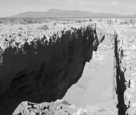 a black and white photo of a canyon in the middle of nowhere with mountains in the background