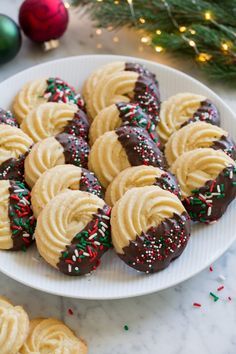 chocolate covered cookies with sprinkles on a white plate next to christmas decorations