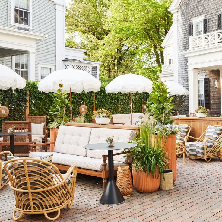 an outdoor living area with wicker furniture and umbrellas on the patio, surrounded by potted plants