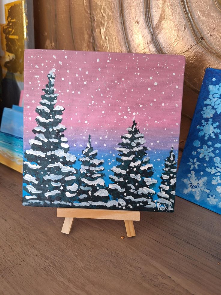 two paintings on easels with snow covered trees in the background