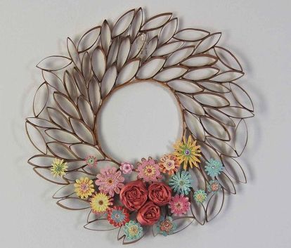 a metal wreath with flowers and leaves hanging on the wall in front of a white wall