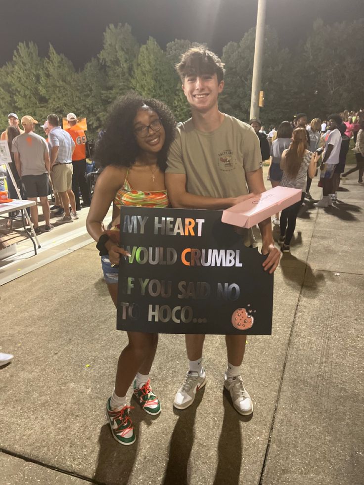 two people standing next to each other holding a sign that says my heart you're cumble if you say it