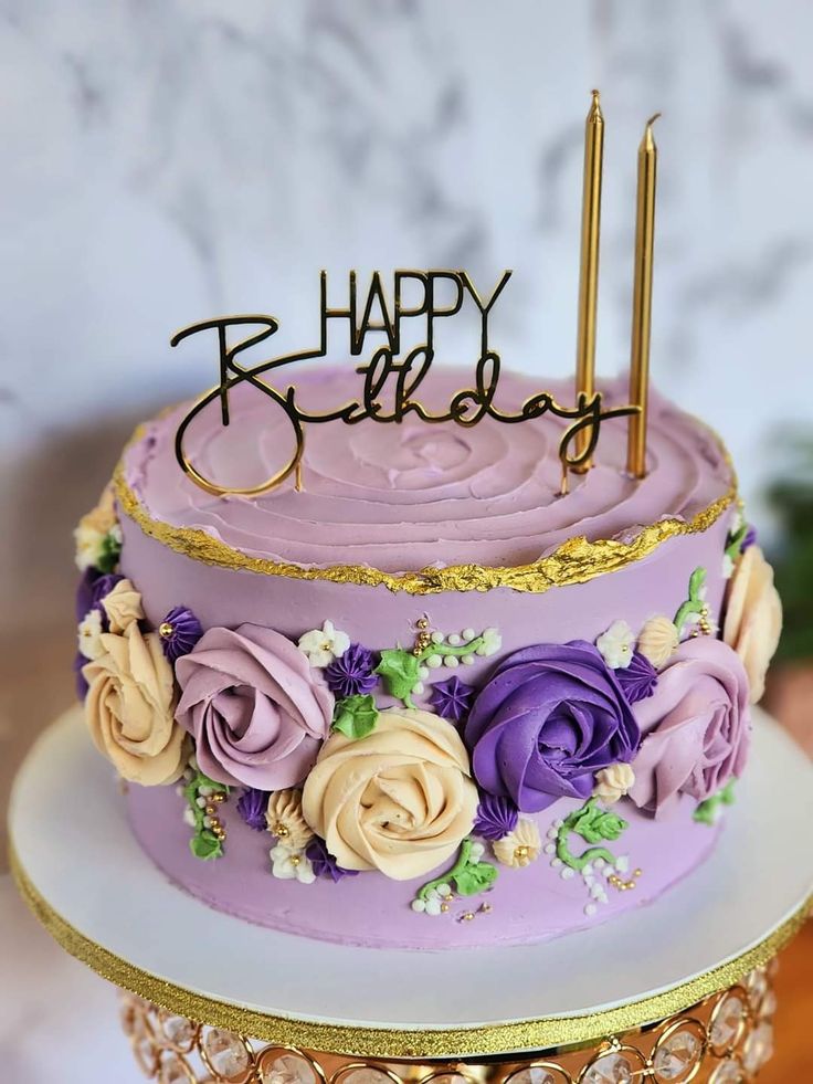 a birthday cake with purple frosting and flowers on the top is sitting on a gold stand