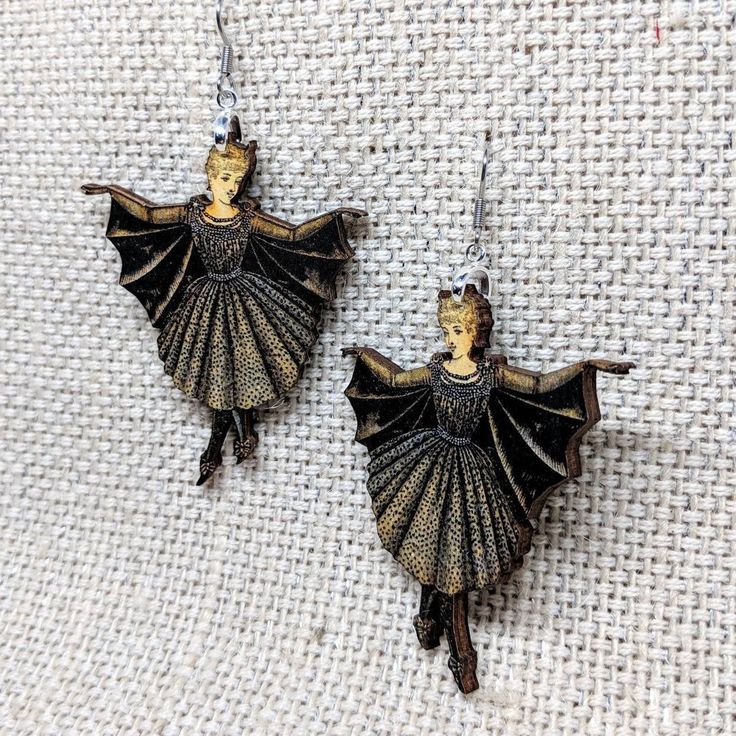 Beautiful Victorian Lady in her elegant bat costume. Pair with our Bat Girl Necklace! • Made in United States • Weight: 0.2 oz (4.5 g) • Measures approx 1.75 x 2 inches • Made of lightweight wood. • Hypoallergenic stainless steel ear wires. • Laser cut and printed with a matte glaze. Bat Jewelry, Bat Girl, Trollbeads Bracelet, Bat Costume, Girl Earrings, Bat Earrings, Laser Cut Earrings, Earrings Halloween, Witch Jewelry