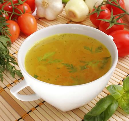 a white bowl filled with soup next to tomatoes, garlic and parsley on top of a bamboo mat