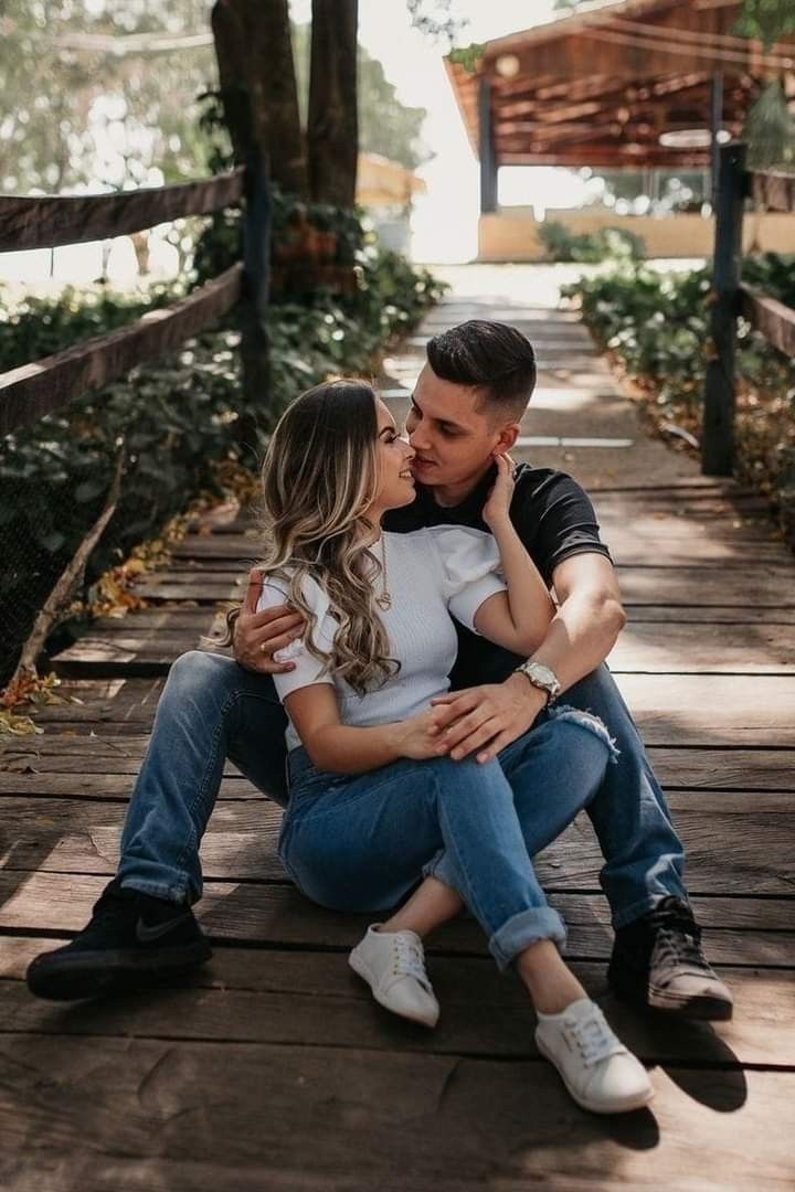 a man and woman sitting on a wooden walkway kissing each other with trees in the background