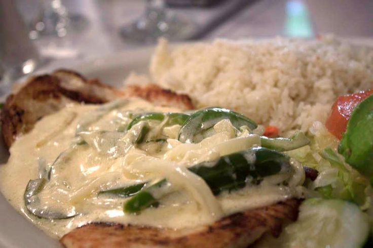 a white plate topped with meat covered in gravy next to rice and veggies