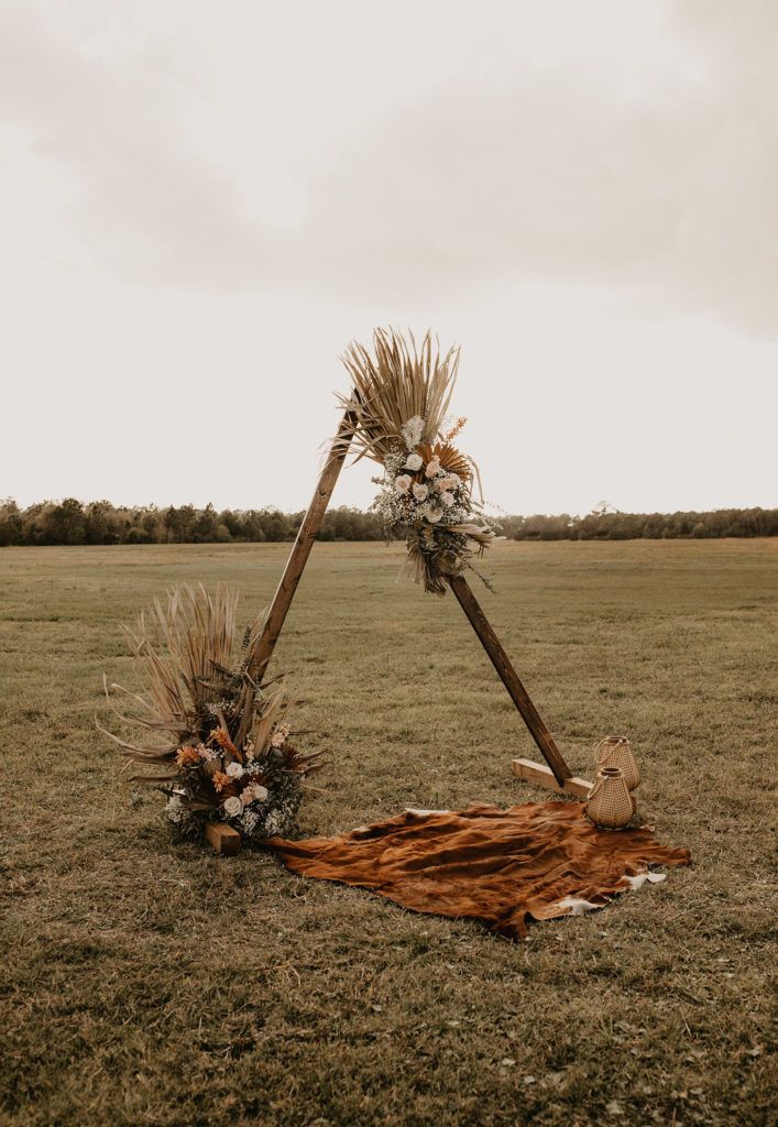 an outdoor ceremony setup with tall grass and flowers on the ground, in front of a cloudy sky