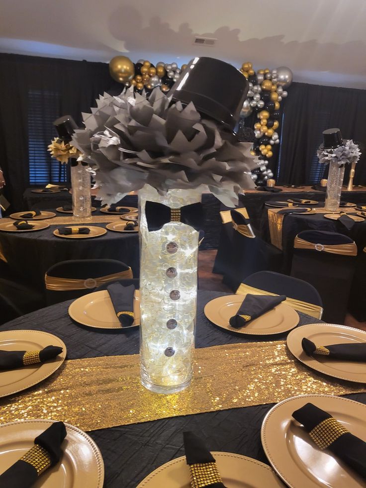 a black and gold table setting with plates, napkins, and flowers in a vase