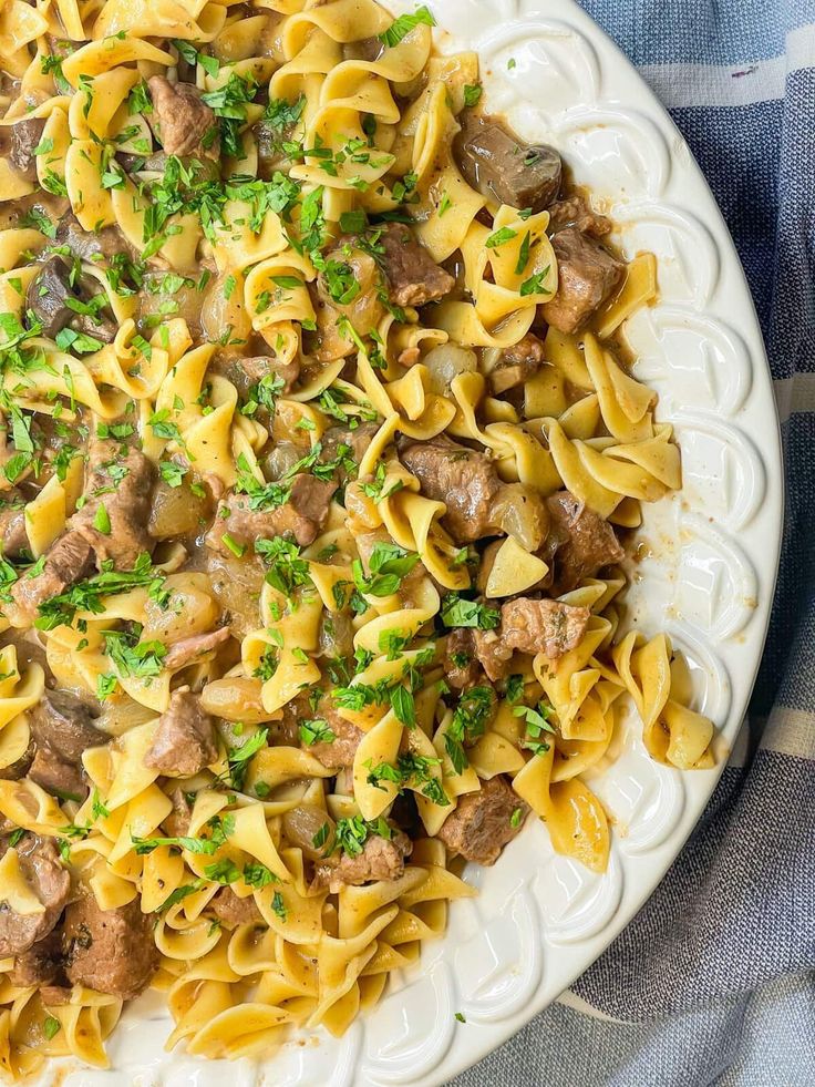 a white plate topped with pasta covered in meat and cheese sauce on top of a blue table cloth