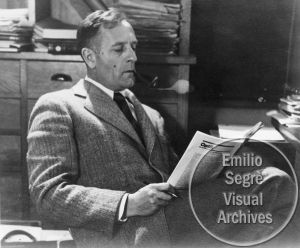 black and white photograph of man in suit reading from the book entitled visual archivess