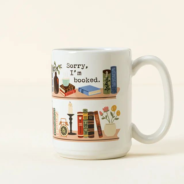 a white coffee mug with books on it and the words sorry, i'm booked