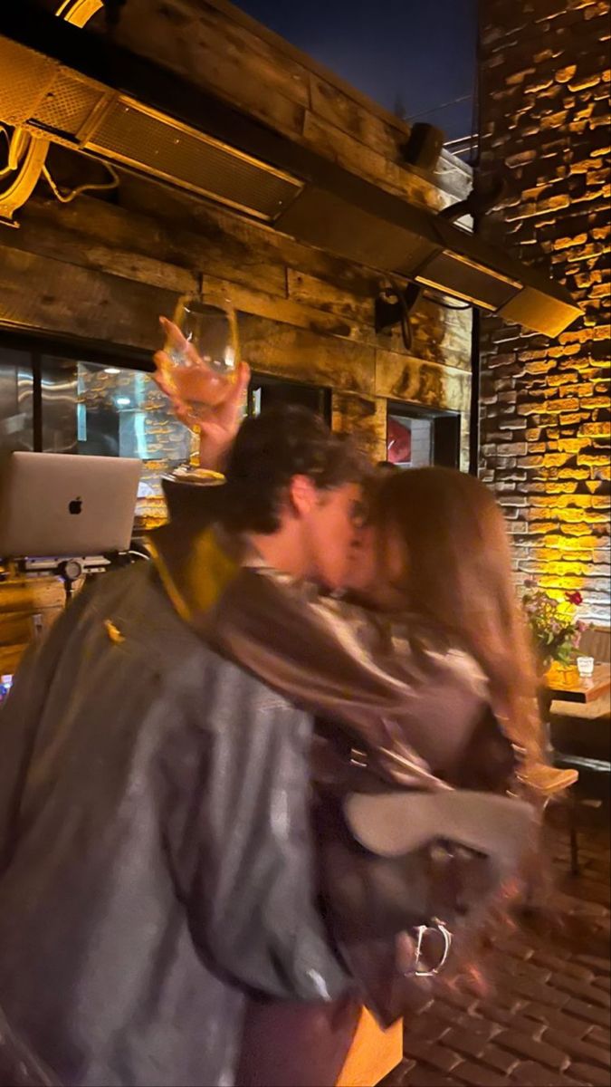 a man and woman kissing in front of a laptop computer on a wooden table next to a brick wall