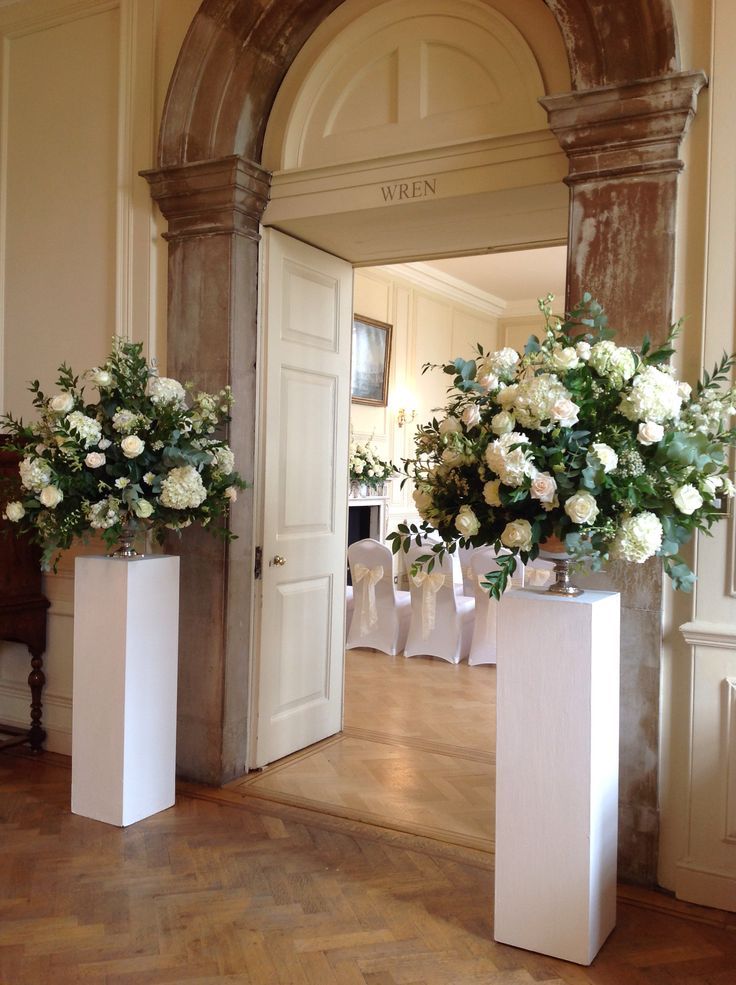 two tall vases with white flowers are on display in front of an open door