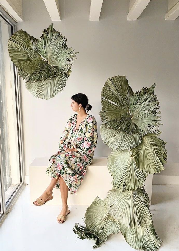 a woman is sitting on a bench next to some large palm fronds that are hanging from the ceiling