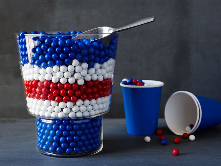 a cup filled with red, white and blue candy balls next to a plastic cup