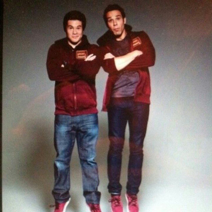 two young men standing next to each other in front of a wall with their arms crossed