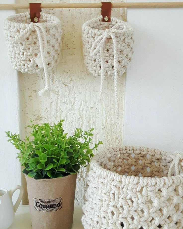 two crocheted baskets on a shelf next to a pot with a plant in it