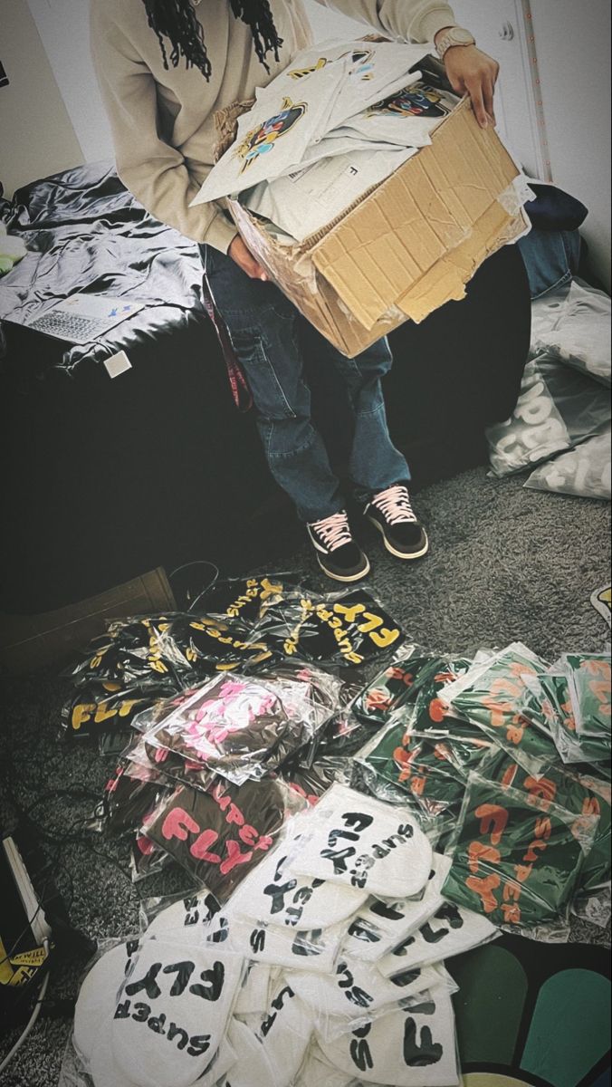 a person sitting on the floor holding a box full of shirts and t - shirts