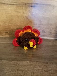 a small crocheted turkey sitting on top of a wooden floor next to a wall