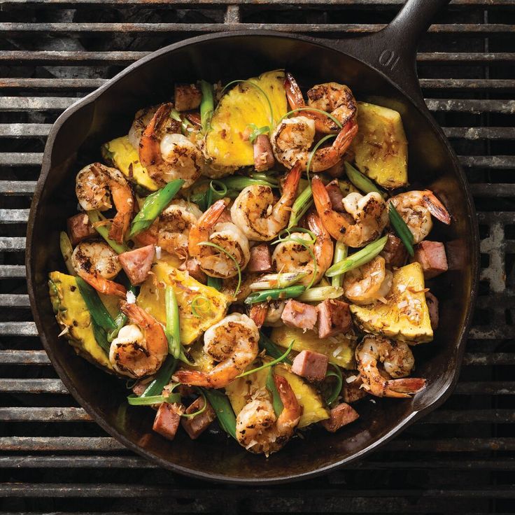 a skillet filled with shrimp, pineapples and green beans on top of a grill