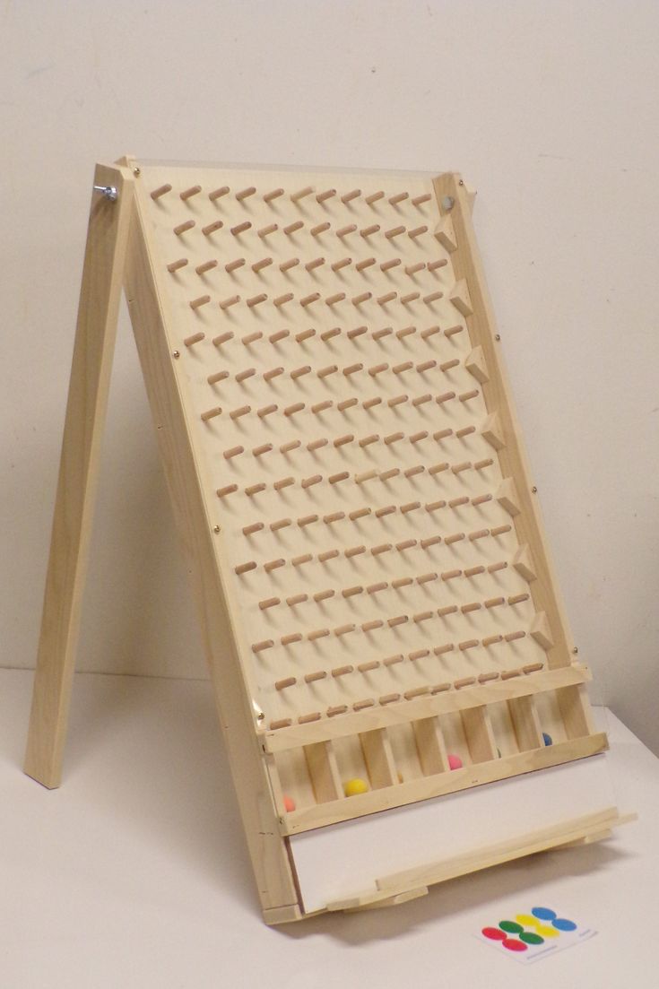 a wooden easel with several pegs in it on a white table next to a wall