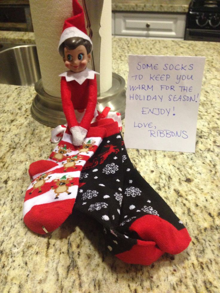 an elf is sitting next to some socks on the counter with a sign that says, come socks to keep you warm for the holiday season