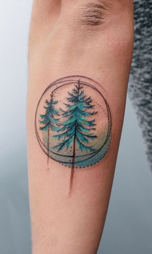 a small tattoo on the arm of a man with pine trees in a snow globe