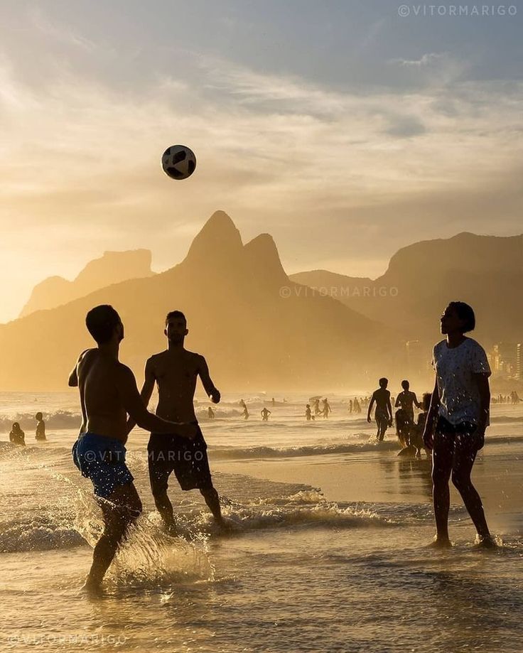 people are playing soccer on the beach at sunset with mountains in the backgroud