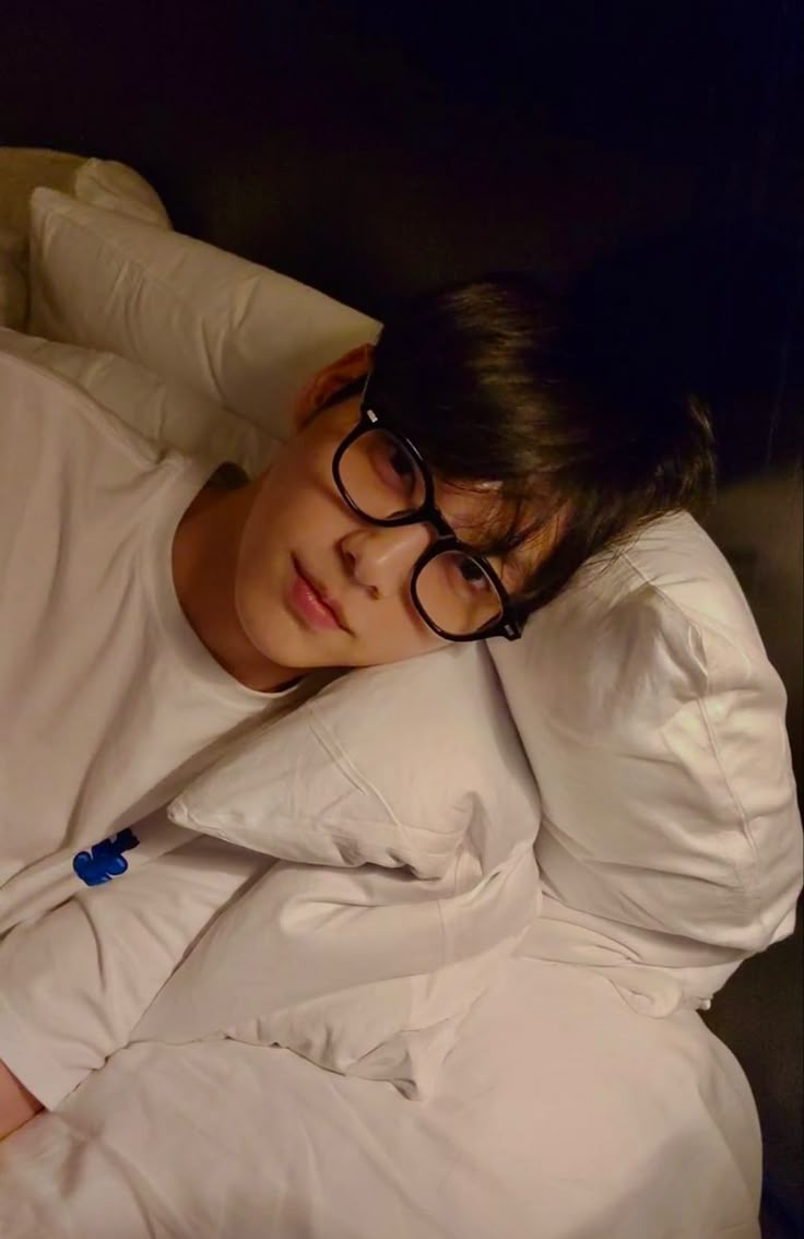 a young man wearing glasses laying on top of a bed