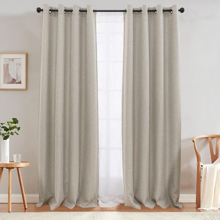 a living room with white walls and beige curtains on the windowsills, along with a wooden chair