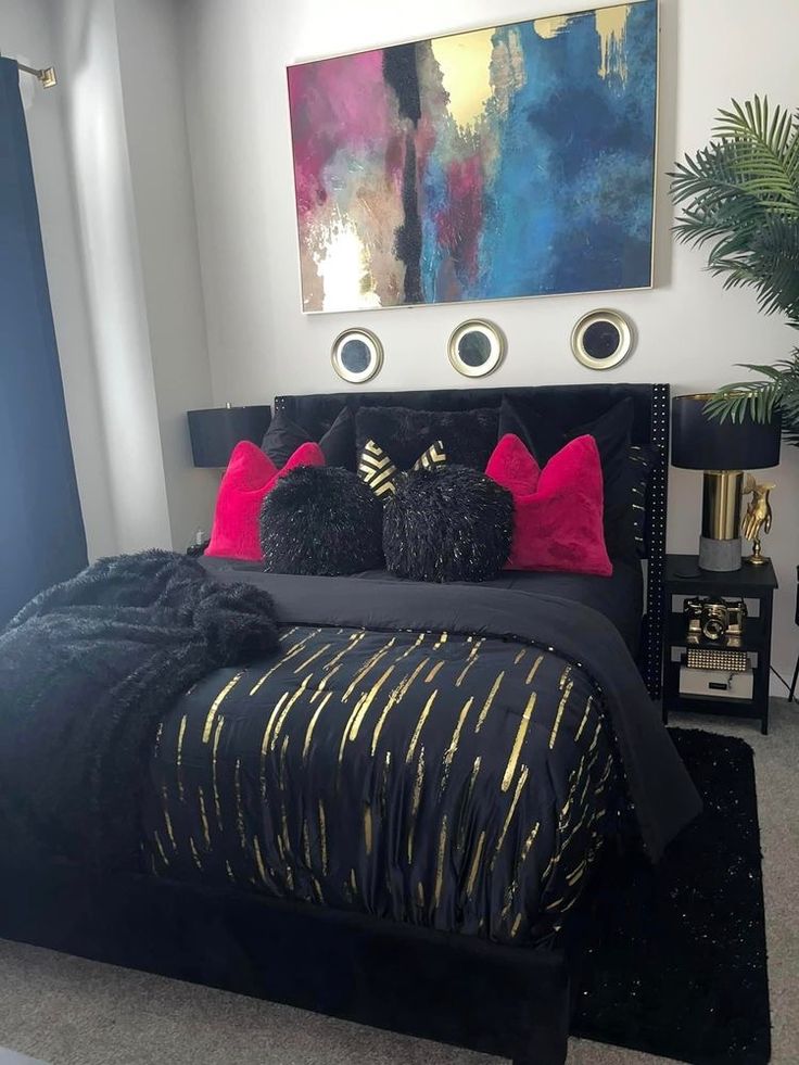 a bedroom with black and gold bedding, red pillows and paintings on the wall