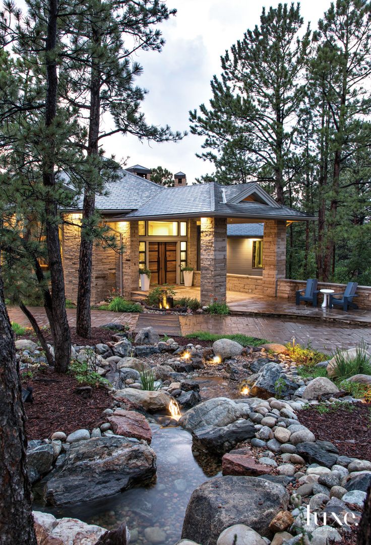 a house in the woods with rocks and lights on it's front porch, surrounded by trees